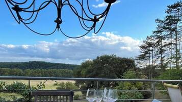 Une table à manger avec de la nourriture et des verres à vin, un lustre et une vue panoramique sur les arbres et les collines.