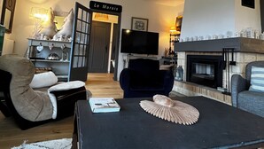 Una sala de estar con chimenea, televisor y un cartel que dice "Le Marais".