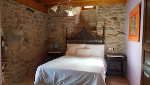 Een slaapkamer met een stenen muur, een houten bedframe, een nachtkastje en een aan de muur hangend schilderij.
