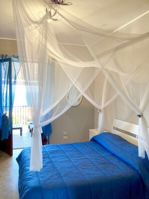 A bedroom with a bed, a nightstand, and a window with sheer curtains.
