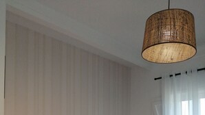 A bedroom with a bed, a bedside lamp, a window with curtains, and a hanging light fixture. - Cozy suite Marina house (Melides)