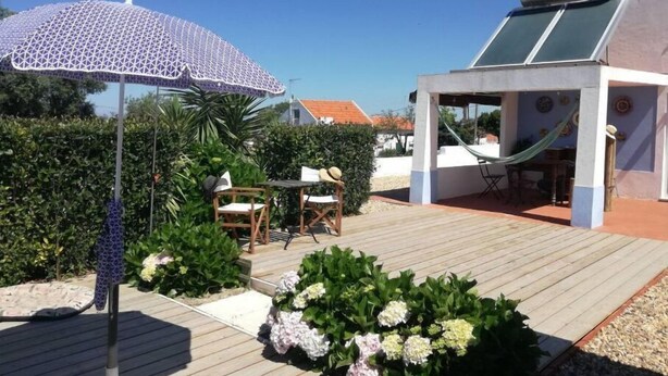 A patio area with a wooden deck, a covered seating area, and a pergola with a white umbrella. - Cozy suite Marina house (Melides)