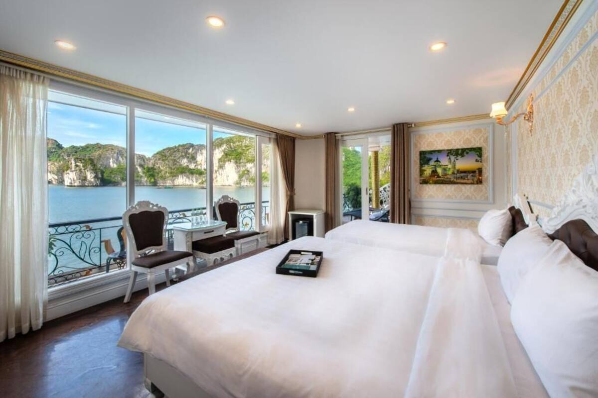 A hotel room with a large bed, a desk, and a chair by a window with a view of cliffs and water.