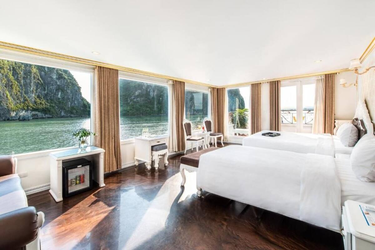 A hotel room with a large window offering a view of a body of water and cliffs, a bed, a small desk with a plant, and a chair.