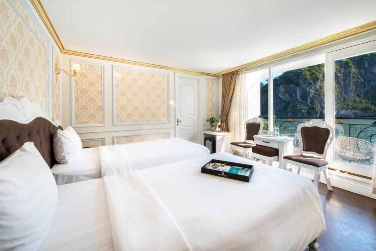 A hotel room with two large beds, a small table with chairs, and a balcony with a scenic view.