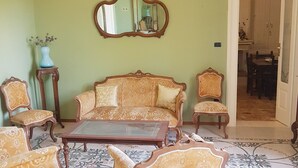 Una habitación con sofá, sillones, una mesa de centro, un espejo y un jarrón con flores.