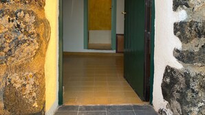 A stone archway leading to a hallway with a tiled floor and a door with a light fixture above it.