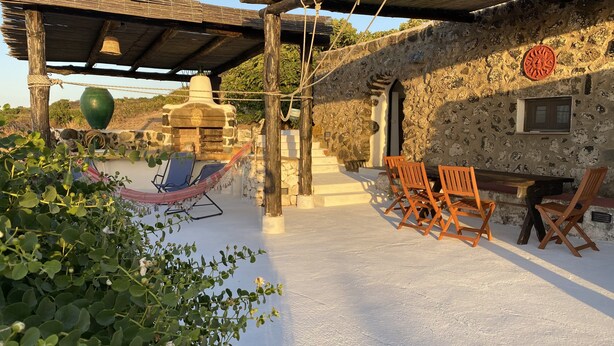A rustic outdoor seating area with a hammock, wooden chairs, and a stone wall.