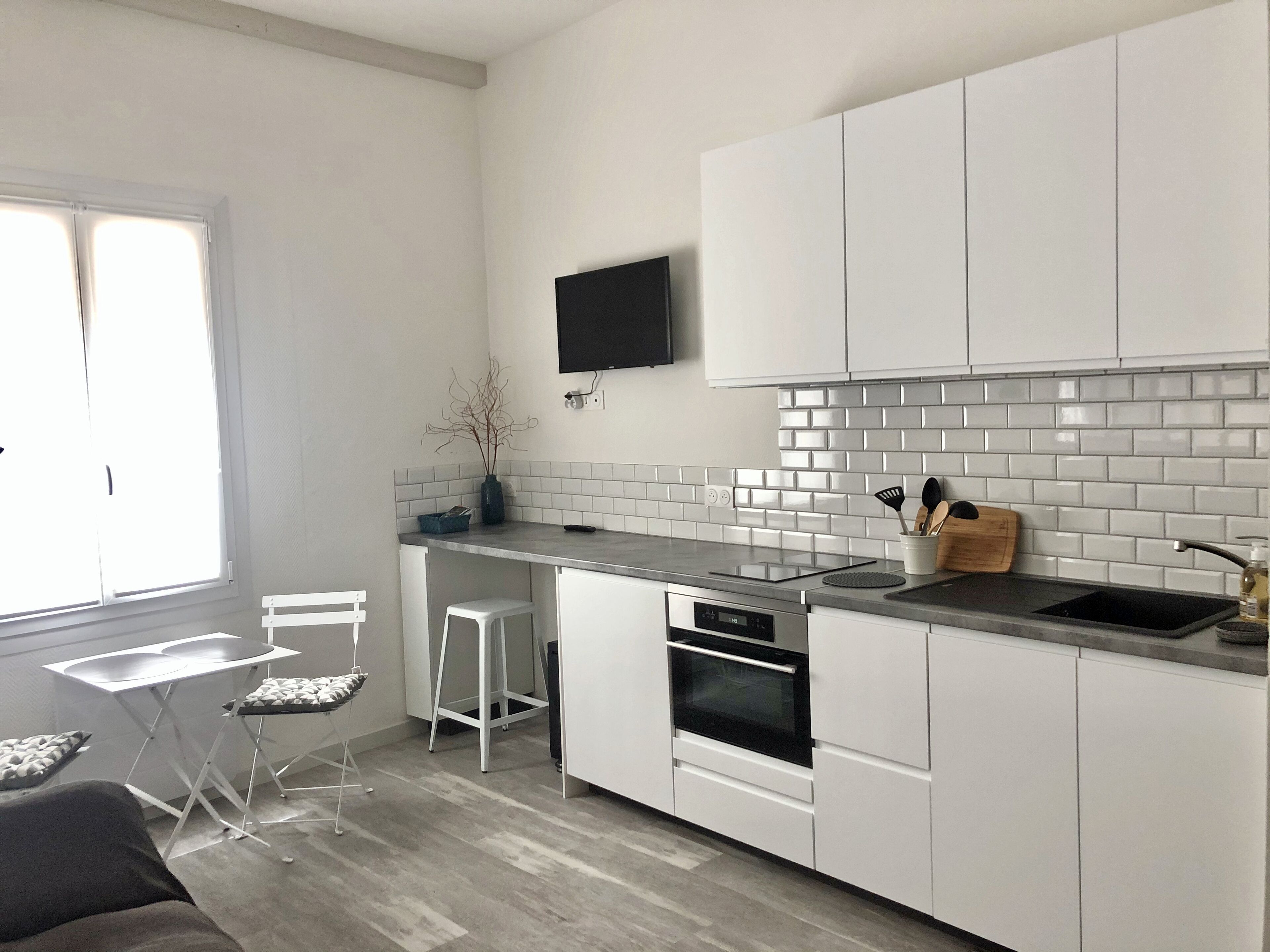 A modern kitchen with white cabinets, a black countertop, a built-in oven, and a TV mounted above the counter.