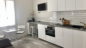 A modern kitchen with white cabinets, a black countertop, a built-in oven, and a TV mounted above the counter. - Apartment Trouville center (rue des Bains), near beach & casino (Trouville-sur-Mer)