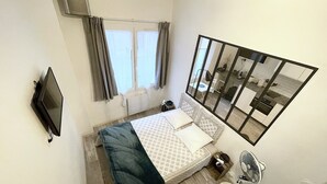 A bedroom with a bed, a TV, a fan, and a window with curtains. - Apartment Trouville center (rue des Bains), near beach & casino (Trouville-sur-Mer)