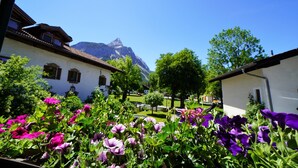 Une cour agrémentée de fleurs aux couleurs vives, de bâtiments traditionnels et, en arrière-plan, d’une montagne.