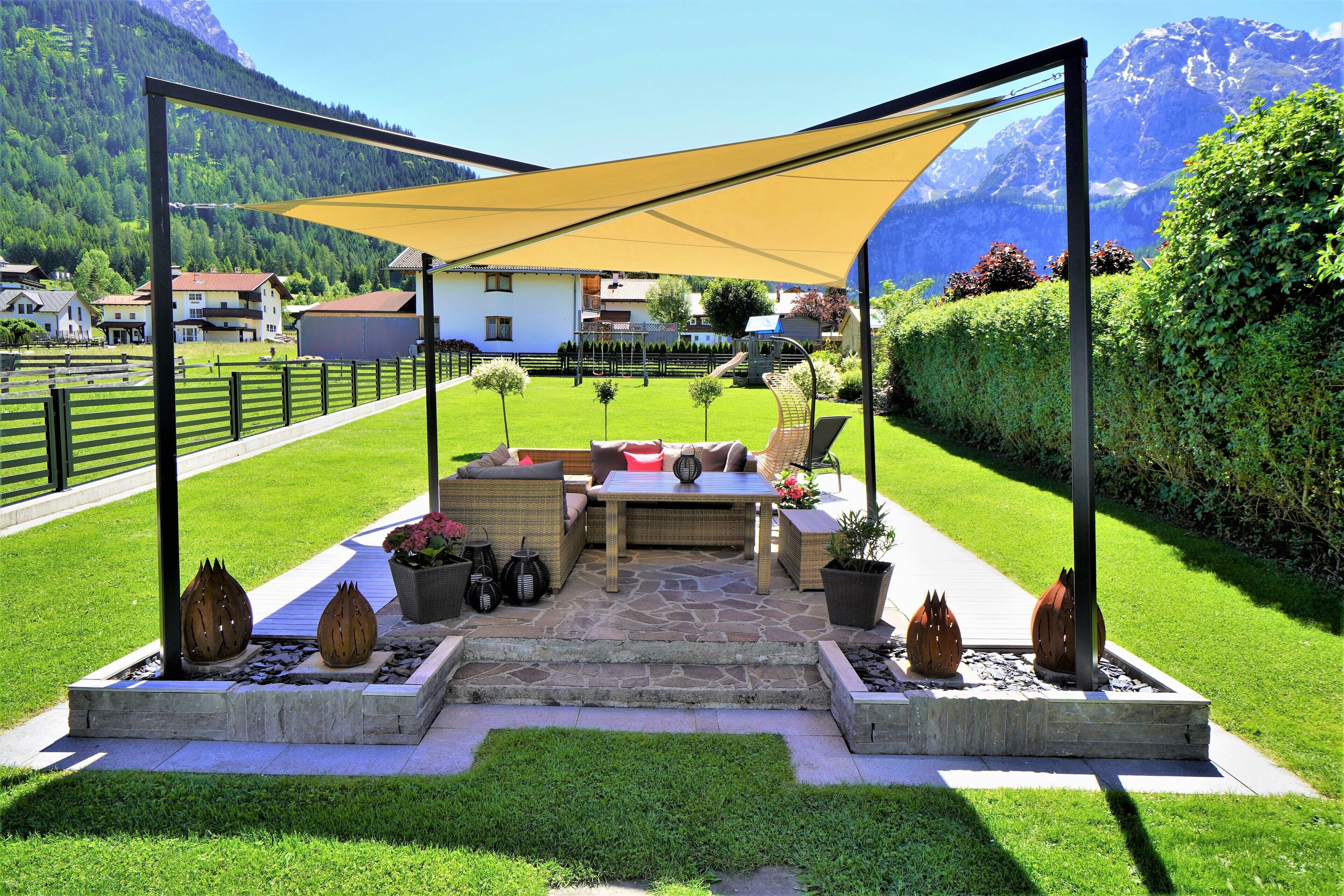 An outdoor patio with a table and chairs, surrounded by a stone floor, and a large canopy providing shade.