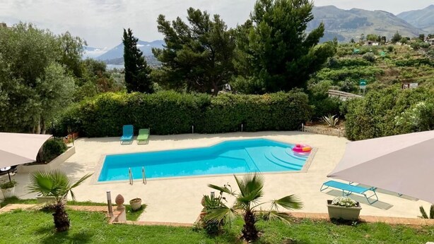 A swimming pool with lounge chairs and a shaded area, surrounded by greenery and mountains in the background. - Villa Flore - Loft - (Casteldaccia)