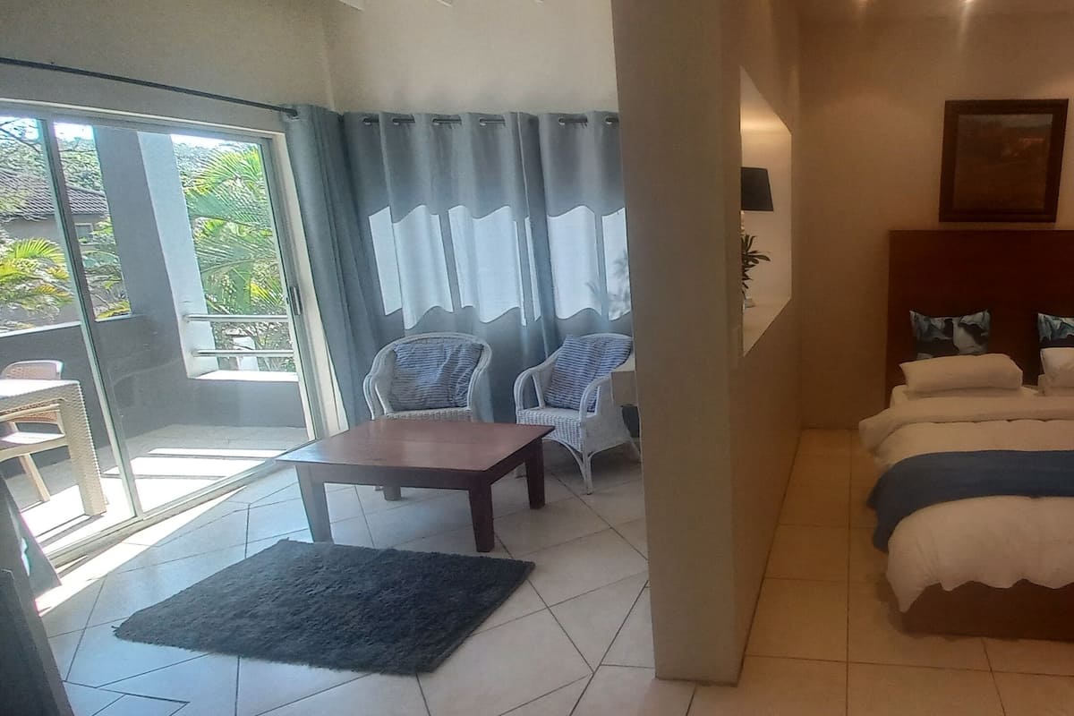 A hotel room with a bed, a small table, two chairs, and a view through a glass door.