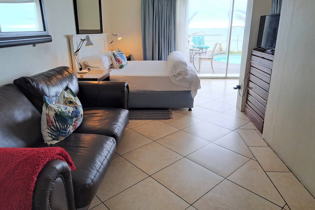 A hotel room with a bed, a sofa, a TV, and a view of the sea.