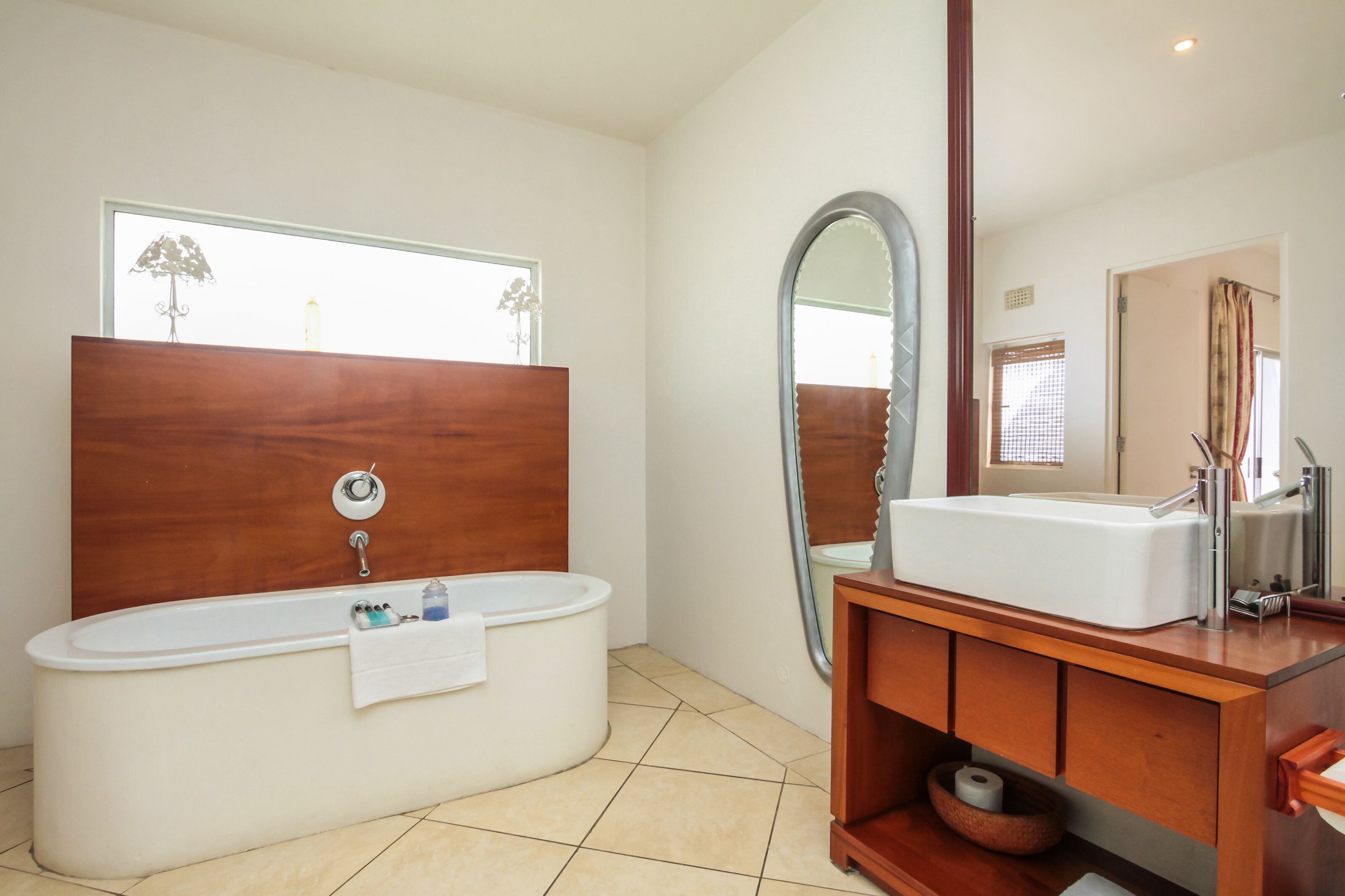 A modern bathroom with a freestanding bathtub, a large mirror, and a wooden vanity with a sink.