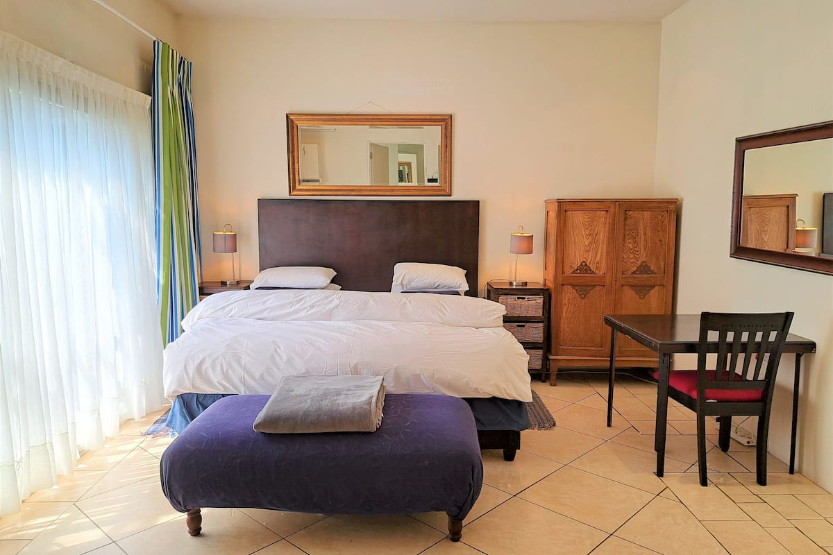 A hotel room with a large bed, a wooden wardrobe, a desk with a chair, and a mirror on the wall.