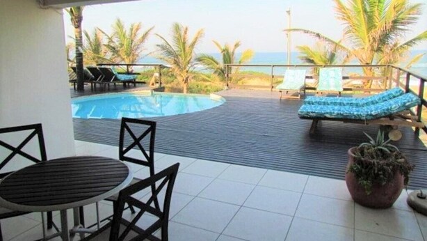 A covered outdoor area with a pool, lounge chairs, and a table. - Bentley On The Beach (Durban North)