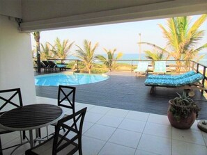A covered outdoor area with a pool, lounge chairs, and a table. - Bentley On The Beach (Durban North)
