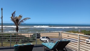 A deck with two lounge chairs, a palm tree, and a view of the ocean with waves and a ship in the distance. - Bentley On The Beach (Durban North)