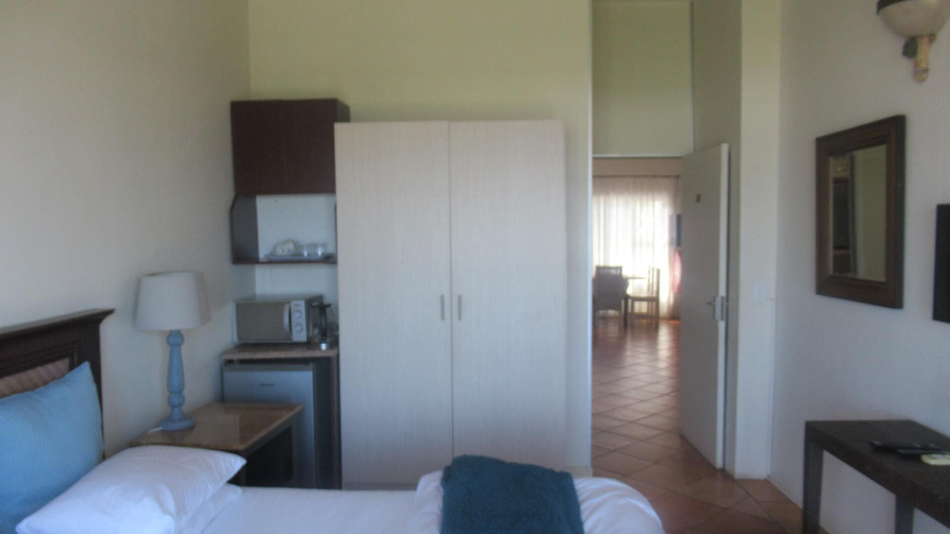 A hotel room with a bed, a desk with a lamp, a microwave, and a wardrobe.