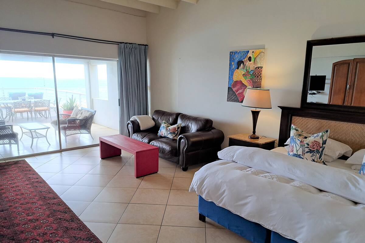 A hotel room with a bed, a sofa, a small table, a lamp, and a painting on the wall.