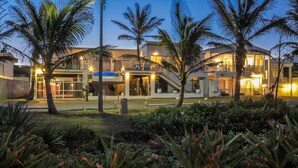 A modern hotel with a covered outdoor area, palm trees, and a well-lit entrance. - Bentley On The Beach (Durban North)