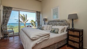 A bedroom with a large bed, a nightstand, a chair, and a view of the ocean. - Bentley On The Beach (Durban North)