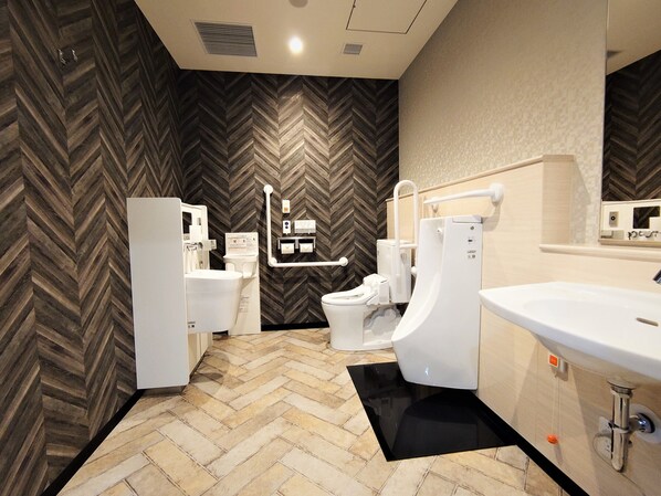 A modern bathroom with a herringbone-patterned wall, a white sink, a toilet, and a bidet. - Green Rich Hotel Nagoya Nishiki Artificial Hot Spring Futamata Yunohana (Nagoya)
