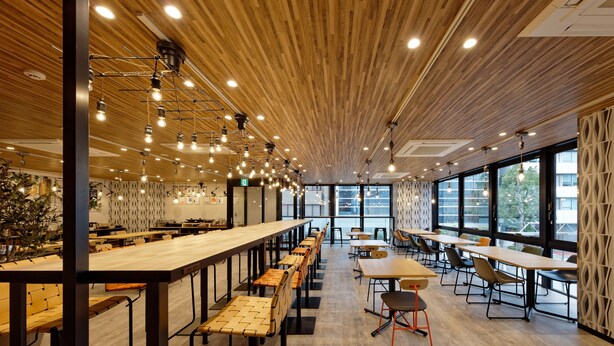 Un comedor moderno con mesas comunitarias largas, asientos individuales y techo de madera.
