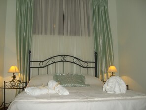 Una cama bien hecha con sábanas y almohadas blancas, dos lámparas de noche y cortinas verdes traslúcidas.