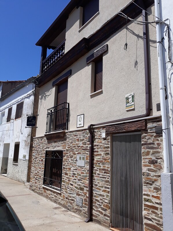 Un edificio de dos pisos con fachada de piedra, un balcón con barandilla de hierro forjado y un gran portón metálico.