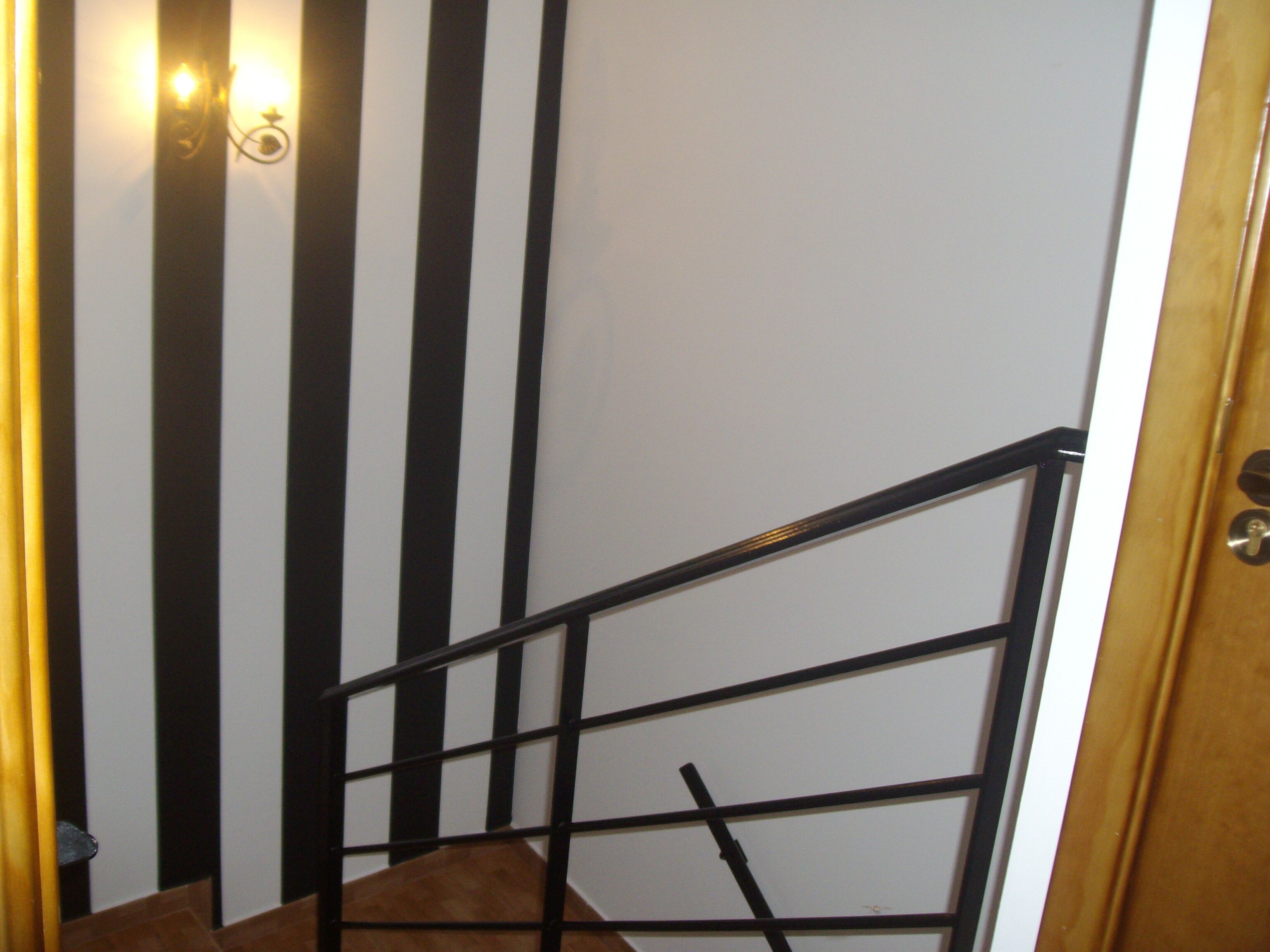 Eine Treppe mit schwarz-weißen Streifen an den Wänden, einer Metallhandläufe und einer Holztür.