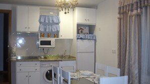 A compact kitchen with a microwave, oven, and washing machine. There is a dining table with chairs and a chandelier above. - Rural House TR-CC-00153 Cerezo Norte Cáceres Region Tierras Granadilla-Cáparra (Cerezo)