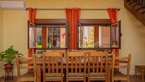 A dining area with a wooden table and chairs, a potted plant, and a window with orange curtains. - Almenas del Cid rural house (Almonacid de Toledo)