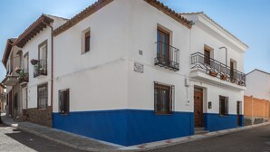 A two-story building with a white facade and blue trim, featuring a balcony with black railings and potted plants. - Almenas del Cid rural house (Almonacid de Toledo)