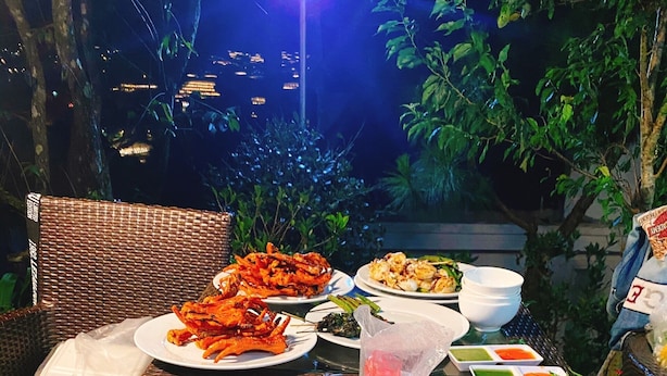 Mesa al aire libre con diversos platos, incluyendo mariscos y verduras, y vista a la ciudad de noche.