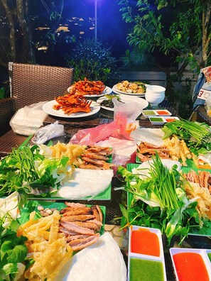 A table set outdoors with various dishes, including seafood and vegetables, and a view of a cityscape at night. - Dallas Hotel DaLat (Xuan Truong - Da Lat)