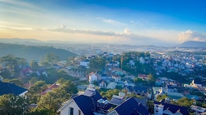 Une vue panoramique d’une ville où se côtoient des bâtiments résidentiels et commerciaux, le tout entouré de collines et surplombé par un ciel dégagé.