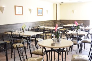 A restaurant with multiple round tables and black metal chairs, featuring framed pictures on the walls.