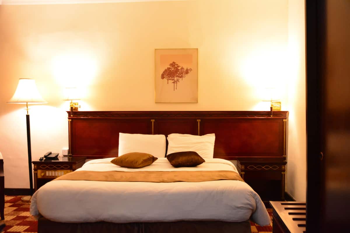 Una cama bien hecha con almohadas blancas y marrones, un cabecero de madera y un cuadro en la pared.