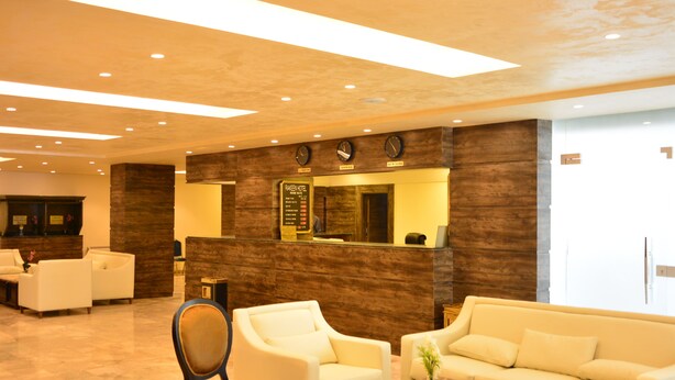 Een hotel lobby met een receptiebalie, een zithoek en een wand met houten accenten.