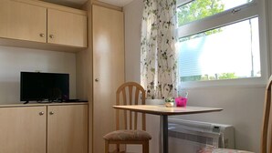 A small kitchenette with a TV, a table with chairs, and a window with curtains. - Chaletparc Krabbenkreek (Sint-Annaland)