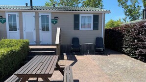 A small, single-story building with numbered doors, a picnic table, and two chairs. - Chaletparc Krabbenkreek (Sint-Annaland)
