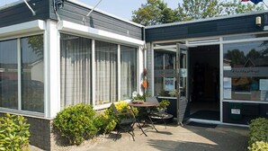 A building with large windows, a small patio with a table and chairs, and a sign that reads "Kleinstock." - Chaletparc Krabbenkreek (Sint-Annaland)
