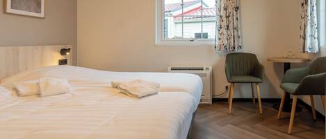 A hotel room with a large bed, a desk with two chairs, a window with curtains, and a radiator.