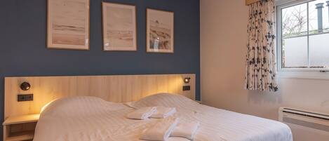 A bedroom with a bed, bedside tables, a window with curtains, and wall-mounted artwork.