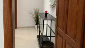 Un couloir avec une porte en bois, une petite table avec un miroir, une plante en pot et un panier pour animal de compagnie.