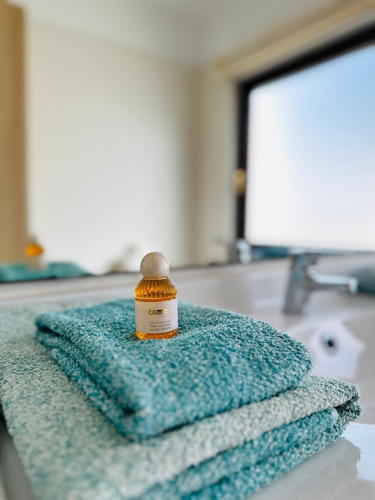A bathroom with a blue towel and a bottle of Touch Clinic bath shower gel on a counter.